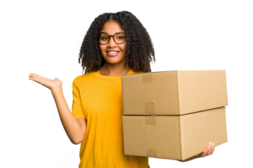 Young african american woman moving to other house while picking up a box full of things isolated showing a copy space on a palm and holding another hand on waist.