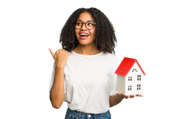 Young african american woman moving to a new home while picking up a box full of things isolated points with thumb finger away, laughing and carefree.