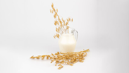 Oat milk in a jug and oat spike on light background. Vegan non dairy alternative milk.