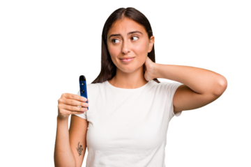 Young caucasian woman holding a electronic cigarette touching back of head, thinking and making a choice.