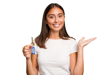 Young caucasian woman holding a home keys isolated showing a copy space on a palm and holding another hand on waist.