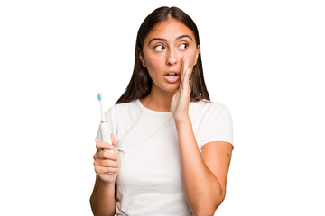 Young caucasian woman holding an electric toothbrush isolated is saying a secret hot braking news and looking aside