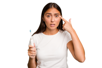 Young caucasian woman holding an electric toothbrush isolated showing a disappointment gesture with forefinger.