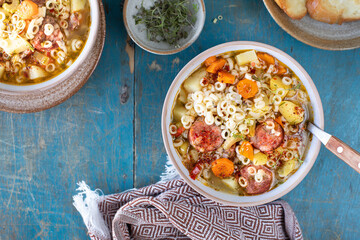 Minestrone soup in a pan on a light table, top view. Italian soup with pasta and seasonal vegetables. Delicious vegetarian food concept.