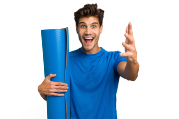Young caucasian sport man holding a mat isolated receiving a pleasant surprise, excited and raising hands.