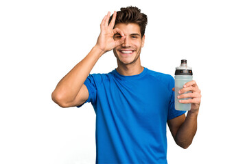 Young sport caucasian man holding a bottle of water isolated excited keeping ok gesture on eye.