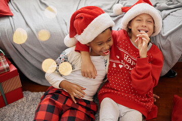 Happy interracial boys wearing festive costumes, Santa Claus hats, licking candy canes, having fun - 545910184