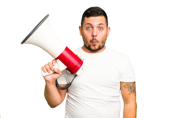 Young caucasian man holding a megaphone isolated shrugs shoulders and open eyes confused.