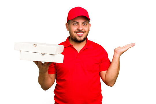 Pizza Delivery Caucasian Man With Work Uniform Picking Up Pizza Boxes Isolated Showing A Copy Space On A Palm And Holding Another Hand On Waist.