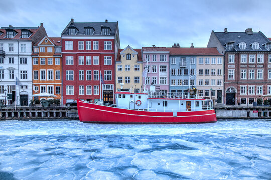 Copenhagen, Denmark - March 2, 2018: The famous Nyhavn pier with colourful buildings and a red boat on the frozen canal. Nyhavn is a waterfront, canal and entertainment district in Copenhagen.