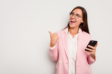 Fototapeta premium Business caucasian woman holding a mobile phone isolated on white background points with thumb finger away, laughing and carefree.