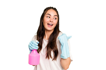 Young cleaner caucasian woman isolated on green chroma background points with thumb finger away, laughing and carefree.