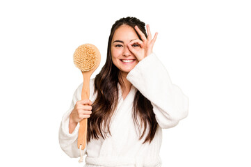 Young caucasian woman holding shower brush isolated on green chroma background excited keeping ok gesture on eye.