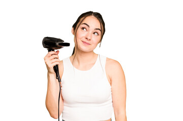 Young caucasian woman holding a hairdryer on green chroma background dreaming of achieving goals and purposes