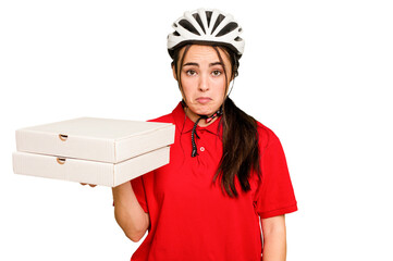 Young caucasian delivery woman holding a pizzas isolated on green chroma background shrugs shoulders and open eyes confused.