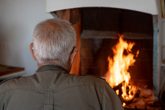 Hombre de espaldas mirando fuego, anciano con ropa de caza, chimenea de suelo antigua de casa rústica