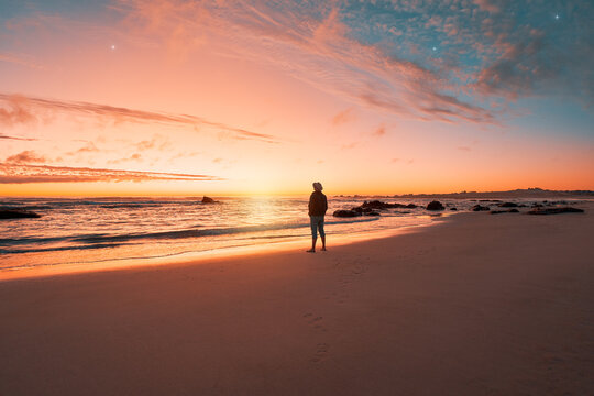 silhouette of a person standing on the shore of the beach looking at and enjoying a beautiful sunset on the horizon