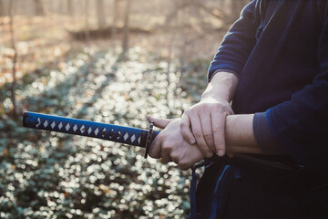 Close up hand with weapon concept photo. Man holding katana. Side view photography with autumn forest on background. High quality picture for wallpaper, travel blog, magazine, article