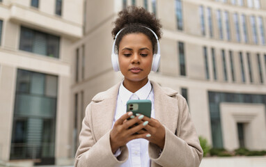 african american stylish woman in headphones on the background of a business center holds a phone in her hands