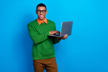 Photo of intelligent clever handsome man wear orange shirt green sweatshirt hold laptop typing email isolated on blue color background