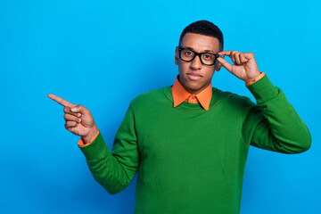 Photo of clever man wear orange shirt under green sweatshirt indicating empty space touch glasses isolated on blue color background