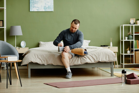 Full Length Portrait Of Adult Man Fixing Prosthetic Leg And Getting Ready To Work Out At Home, Copy Space