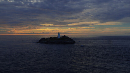Naklejka na ściany i meble Leuchtturm auf Felsen im Meer mit dramatischem Sonnenuntergang
