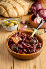Top view of red bean stew on rustic wooden table with spoon, green chillies, garlic, onions, bay leaf and loaf of bread, selective focus, vertical