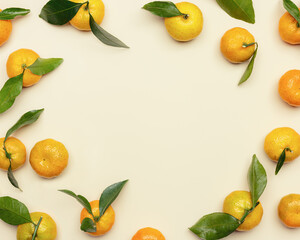 Fresh orange yellow tangerines with green leaves on beige table, round frame with copy space. Citrus fruits mandarines as food background, flat lay style, christmas fruits tangerines
