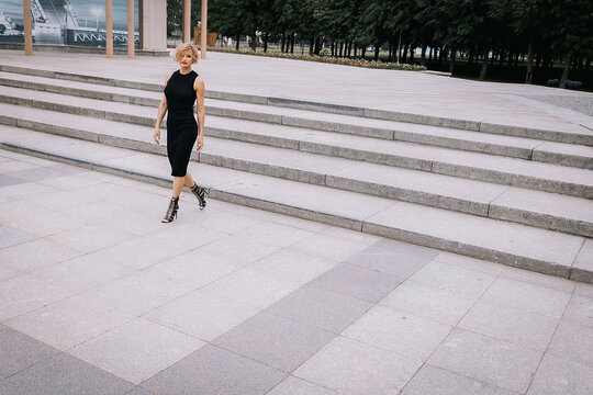 Beautiful woman in black clothes walks up stairs in park. Art shooting from unusual angles. High quality photo