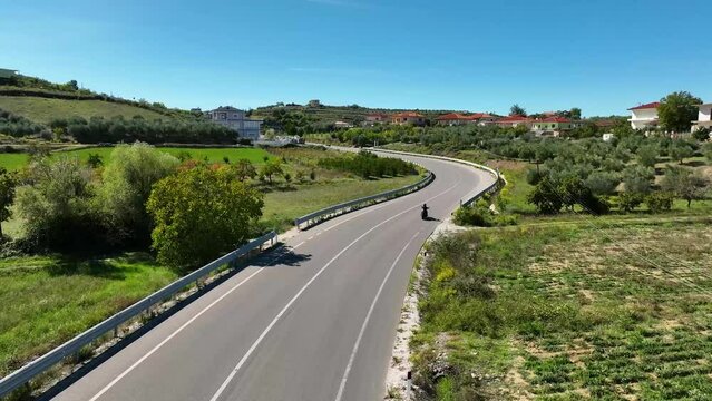 Motorcycle travelling on empty village road near houses and fields on a sunny day areal shot 4K 60fps