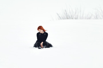Fototapeta na wymiar A sad redhead girl sits in the snow in winter in a large white empty space