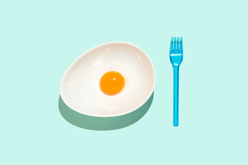 Creative idea a yolk on white bowl and blue fork. An egg for a meal on the blue table. Flat lay.