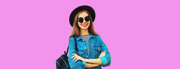 Portrait of happy smiling young woman model wearing black round hat, jean jacket and backpack on pink background, blank copy space for advertising text