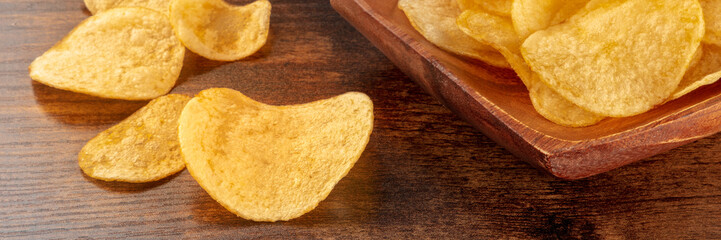 Potato chips or crisps, a salty snack on a wooden background, a panorama