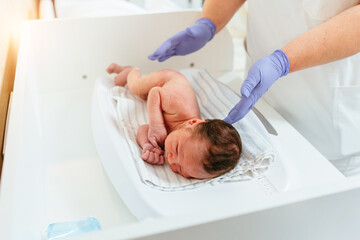 Obraz na płótnie Canvas New born baby boy on a scale. Female doctor weighting cute baby in clinic.