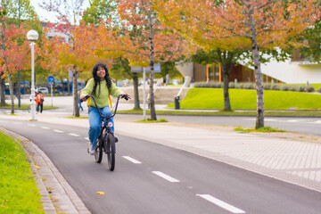 Young asian female student cycling on her way to college in autumn, healthy life, eco friendly