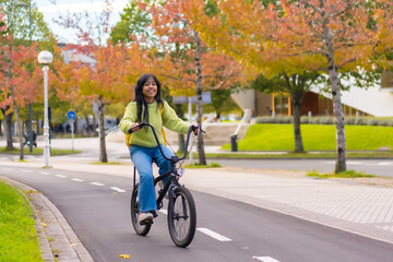 Young Asian female student smiling riding a bicycle on her way to college in autumn, healthy life, eco friendly