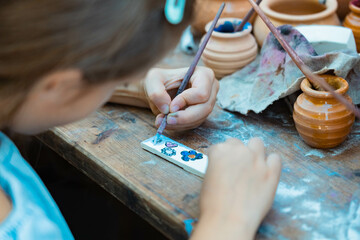 Little girl's hands paint a piece of wood. 5 year old kid decorates with a brush and paints in...