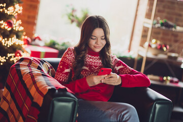 Portrait of nice cute positive smart girl with wavy hairdo dressed red ornament sweater look typing message on phone in house indoors