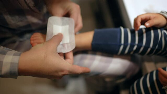 Parent Putting Bandage On Child Feet. Injured Kid After Getting Physically Hurt