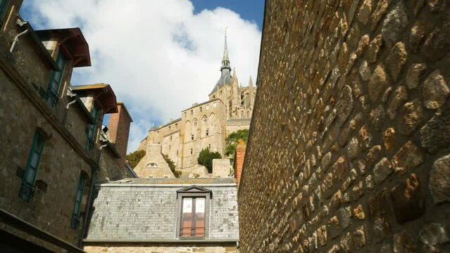 The famous gothic abbey of the Mont Saint Michel, Normandie, France. In the foreground the typical lattice and medieval buildings. Blue sky with white clouds on the background.