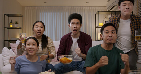 Group of young adult friend man and woman asia people sit at sofa couch joy night party fun game FIFA world cup live TV at home eat snack bowl drink beer bottle glass jump mad happy win exult face
