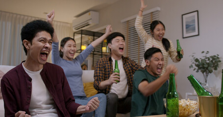 Group of young adult friend man and woman asia people sit at sofa couch joy night party fun game FIFA world cup live TV at home eat snack bowl drink beer bottle glass jump mad happy win exult face