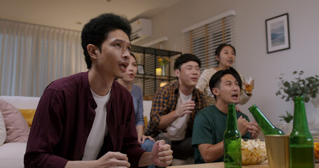 Group of young adult friend man and woman asia people sit at sofa couch joy night party fun game FIFA world cup live TV at home eat snack bowl drink beer bottle glass jump mad happy win exult face