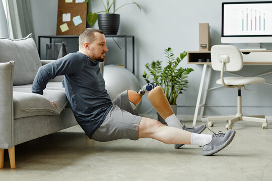 Side view portrait of man with prosthetic leg doing exercises at home in minimal interior