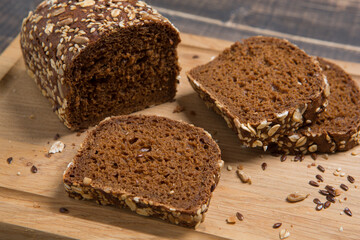 Loaf of brown bread, partially cut into pieces, with flax seeds, sunflower seeds and oatmeal, on a cutting board