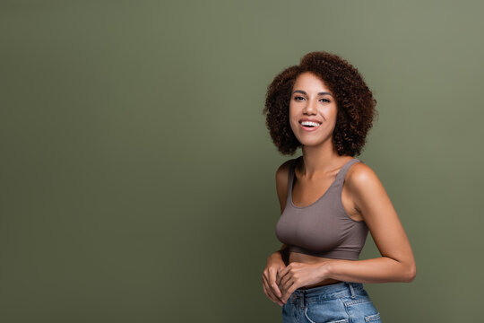Pretty african american woman in top and jeans looking at camera isolated on green.