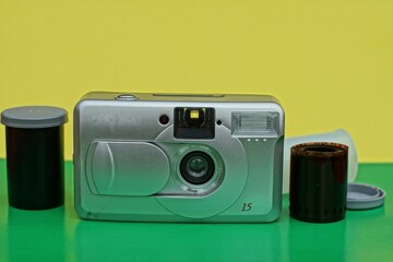 old technologies.Amateur camera for color film plastic silver color together with the used film stands on a green surface on a yellow background