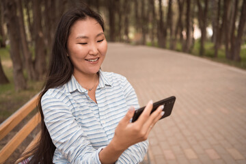 Young asian woman sitting in city park and using phone for video call